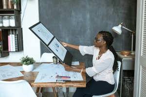 A professional woman analyzes design plans at her workspace, utilizing technology for a creative project.