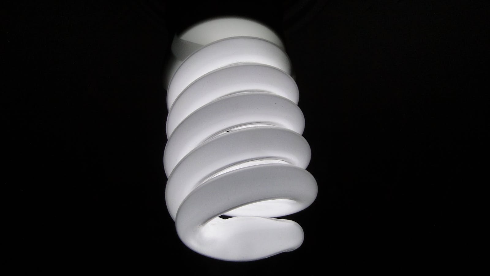 Detailed view of a spiral fluorescent light bulb on a black background.
