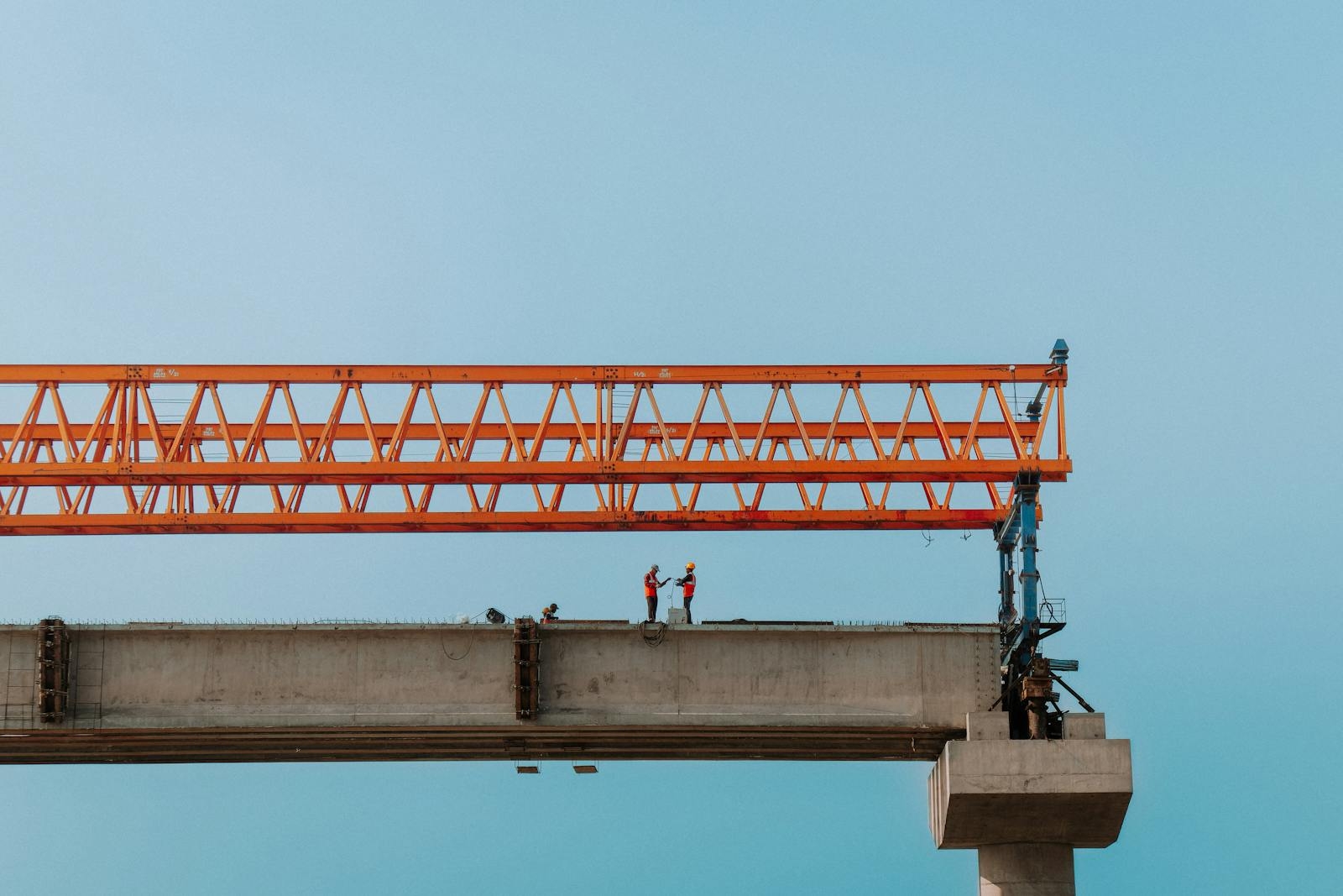 Construction workers on an elevated bridge in Chilmari, Bangladesh against a clear sky.