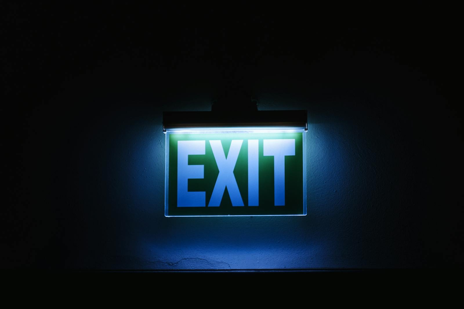 Photo of a glowing green exit sign in a dark environment, symbolizing safety and direction.