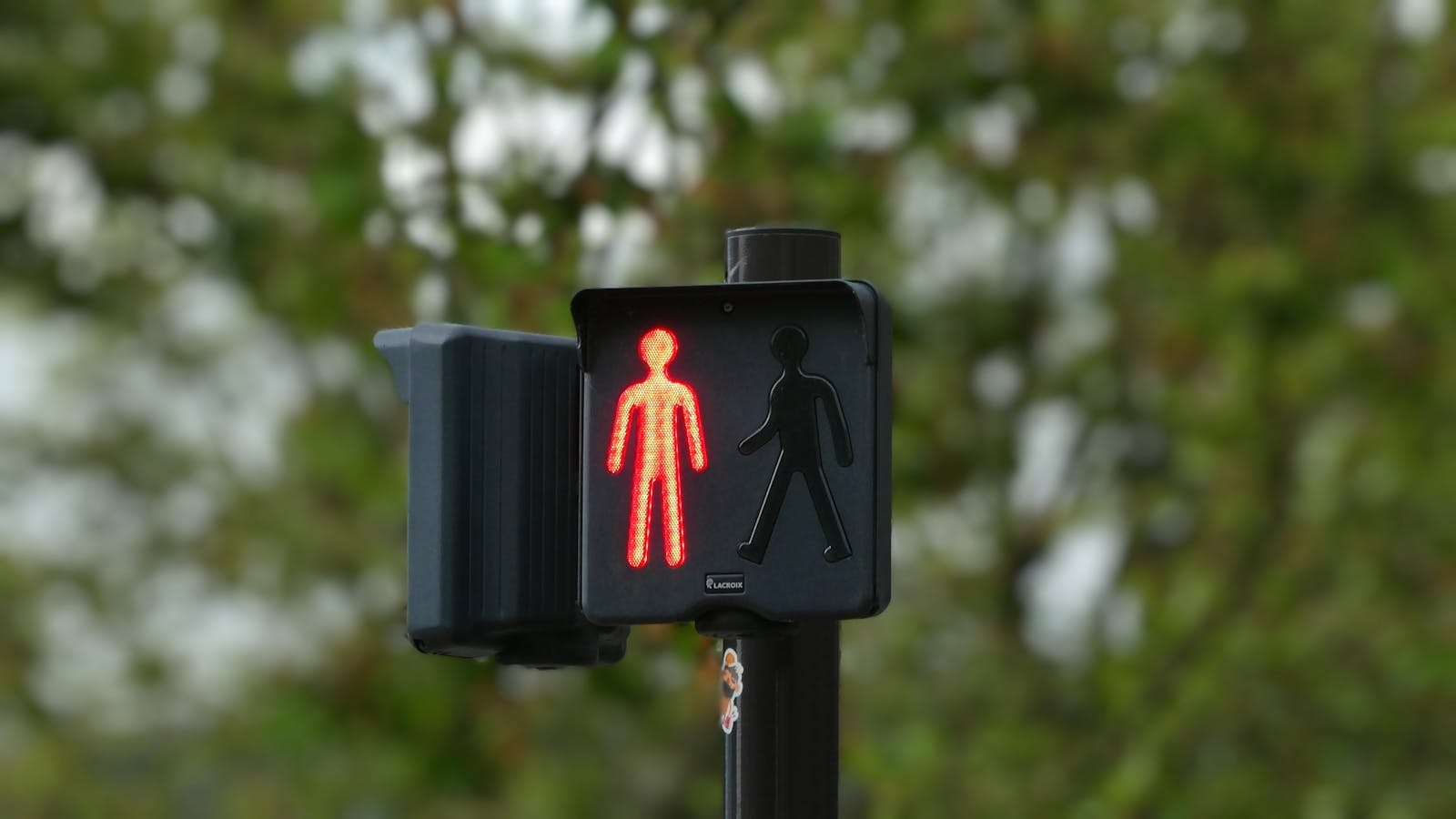Red pedestrian signal against a blurred green background, symbolizing stop.