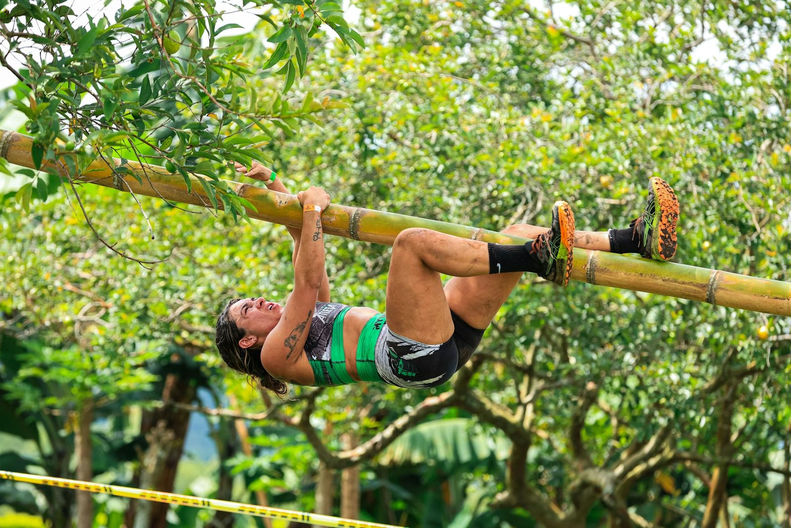 Woman athlete tackling a bamboo climb in an outdoor adventure race under a lush canopy.