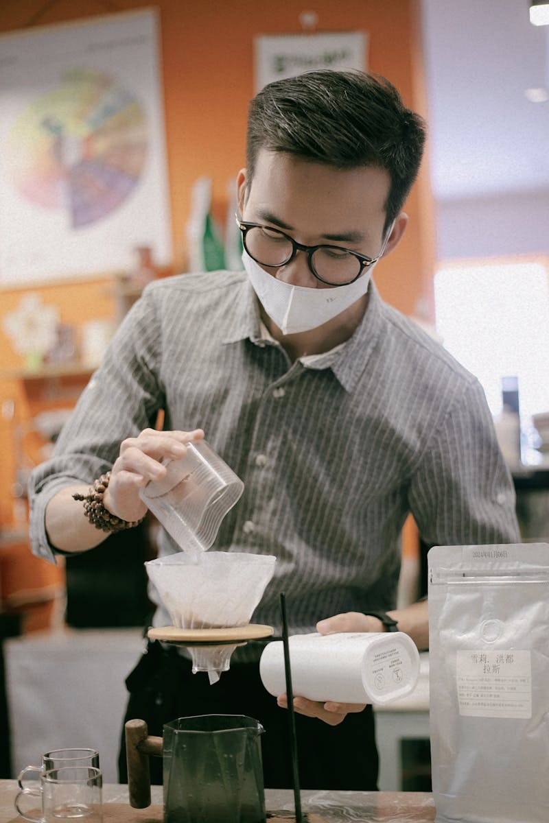 Barista prepares pour over coffee in trendy cafe setting, focusing on craftsmanship.