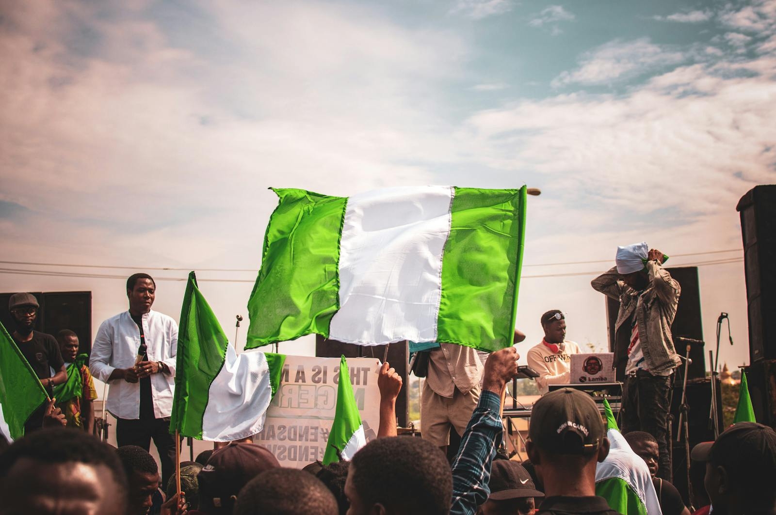 A vibrant gathering of people holding Nigerian flags outdoors under a sunny sky.
