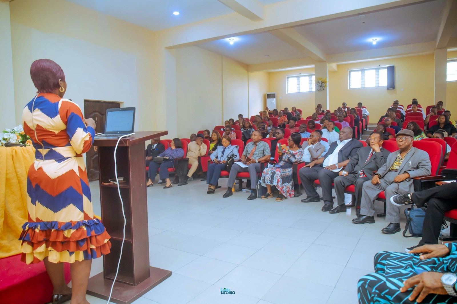 A woman presents to a large audience in an auditorium.