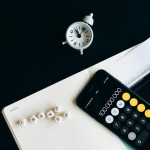 Notebook with an iPhone displaying 100,000,000, desk clock and financial charts suggesting market analysis.