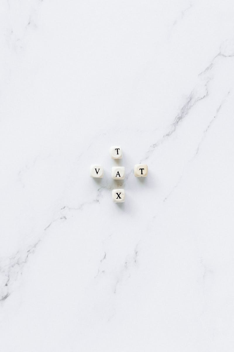 White dice spelling 'Tax' and 'VAT' on a marble surface, symbolizing taxation concepts.