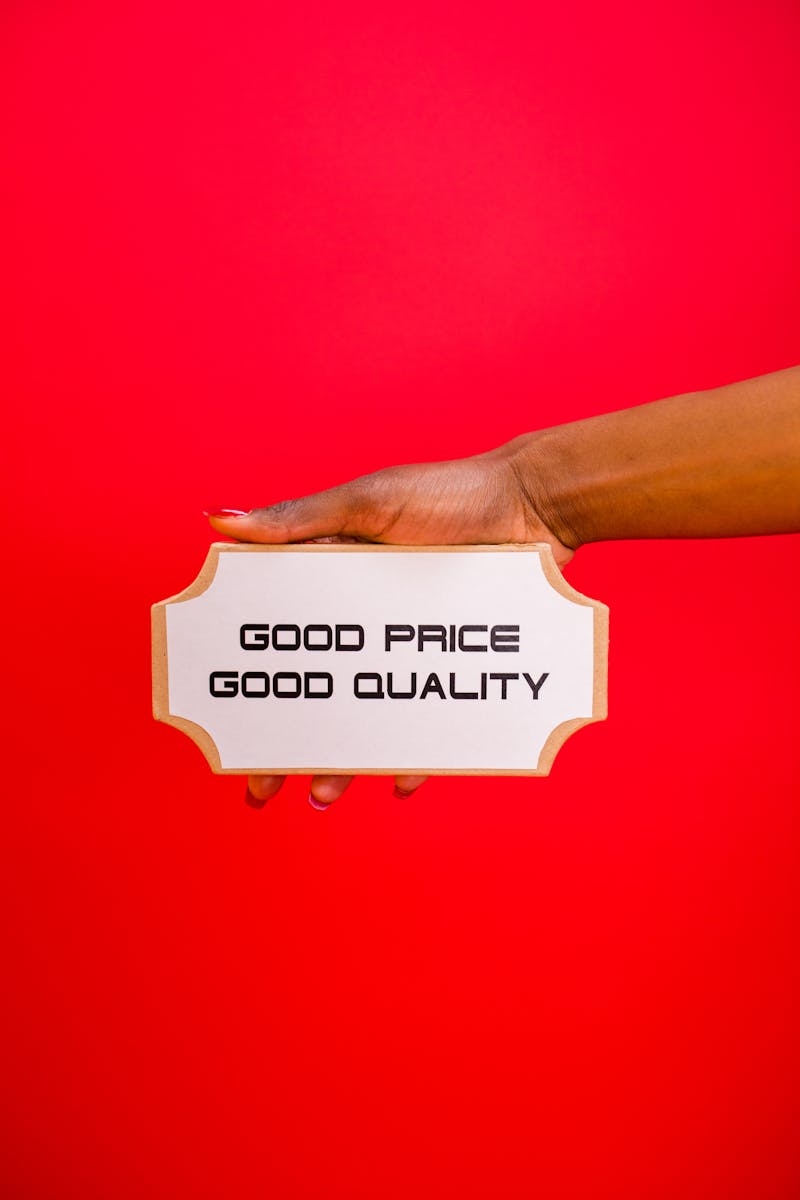 A hand holding a sign with 'Good Price, Good Quality' text against a bright red background.